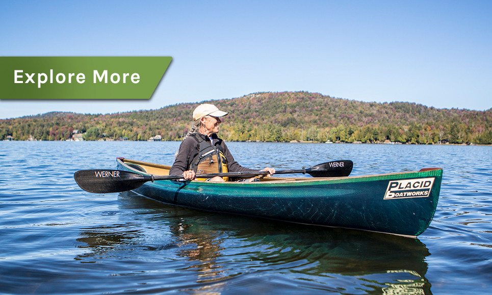 A woman in a green solo canoe with a mountain of fall colors in the background.